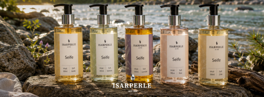 Isarperle Markenshop-Banner – Fünf Flüssigseife-Spenderflaschen à 300ml auf einem Felsstein im Abendlicht an einem Gebirgsfluss: Duft Vanille, Verbene, Lavendel, Rose und Zirbe. Isarperle seit 1856.