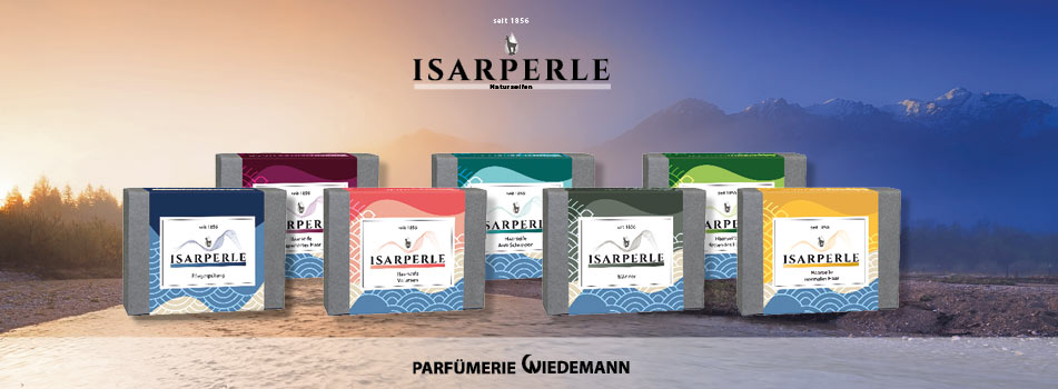 Sieben bunte Naturseifen der Marke Isarperle sind vor einer Berglandschaft bei Sonnenaufgang arrangiert. Darüber das Logo „Isarperle Naturseifen“ und unten der Schriftzug „Parfümerie Wiedemann“.