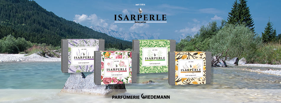Vier bunte Seifenstücke der Marke Isarperle stehen auf einem Stein in einem klaren Gebirgsfluss, umgeben von grüner Natur und Bergen. Darüber das Logo „Isarperle Naturseifen“ und unten der Schriftzug „Parfümerie Wiedemann“.