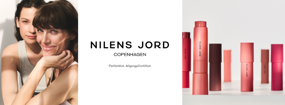 Werbebanner für Nilens Jord Copenhagen: Zwei Frauen lächeln in die Kamera, daneben stehen mehrere farbige Make-up-Sticks der Marke Nilens Jord vor hellem Hintergrund.