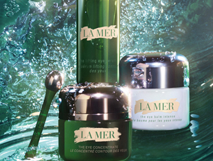 Drei Pflegeprodukte von La Mer vor einem grünen, wasserähnlichen Hintergrund. Im Vordergrund ein grüner Tiegel ‚The Eye Concentrate‘ mit silbernem Deckel und Applikatorstab. Dahinter ein grüner Pumpspender und ein weißer Tiegel ‚The Eye Balm Intense‘.