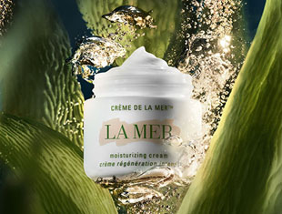 Tiegel der ‚Crème de la Mer‘ schwebt in einer Unterwasserszene zwischen grünen Algen und Luftblasen. Auf dem weißen Tiegel steht: ‚La Mer – moisturizing cream – crème régénération intense‘.
