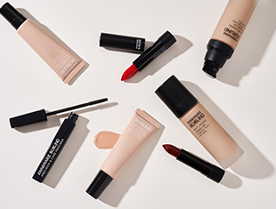 Make-up-Produkte von ANNEMARIE BÖRLIND, darunter Foundation, Lippenstifte und Mascara in Schwarz und Beige, auf hellem Untergrund verteilt.