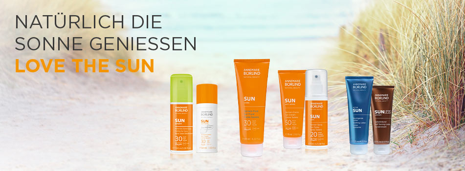 Breites Sortiment an Sonnenschutzprodukten in Orange-Blau, vor natürlichem Küstenhintergrund – Claim: ‚Natürlich die Sonne genießen.