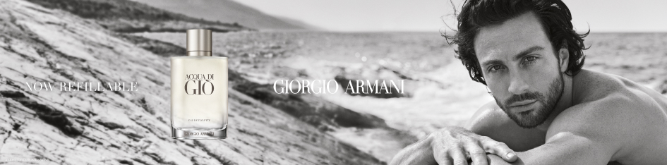 Werbebild für 'Giorgio Armani Acqua di Giò'. In einer schwarz-weißen Strandlandschaft liegt rechts ein muskulöser Mann mit Bart und dunklen Haaren auf einem Felsen und blickt intensiv in die Kamera. Links daneben ist die transparente Parfumflasche mit silberner Kappe und der Aufschrift 'Acqua di Giò – Giorgio Armani' zu sehen. Darüber steht 'Now Refillable'.