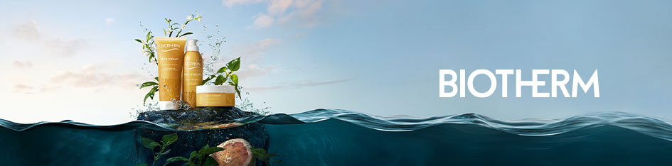 Werbung für Biotherm Pflegeprodukte mit natürlichen Inhaltsstoffen. Drei goldgelbe Produkte stehen auf einem Felsen, der aus dem Wasser ragt, umgeben von Pflanzen und einer aufgeschnittenen Grapefruit. Der Hintergrund zeigt Meer und Himmel bei Sonnenuntergang. Rechts das Biotherm-Logo..