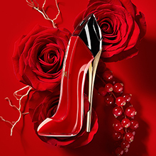 Parfümflakon in Form eines roten High Heels mit schwarzer Spitze und goldenem Absatz, umgeben von Rosenblüten und Perlenketten auf rotem Hintergrund. Beschriftung darunter: 'Very Good Girl'.