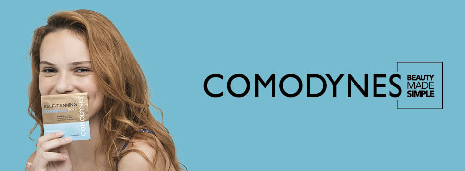 Junge Frau mit langen, rötlich-blonden Haaren hält ein Comodynes Self-Tanning Tuch vor ihr Gesicht und lächelt. Rechts daneben der Markenname COMODYNES mit dem Slogan 'Beauty Made Simple' auf hellblauem Hintergrund.