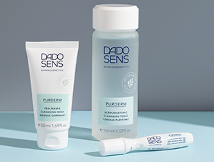 Pflegeserie für unreine Haut und Akne, dargestellt auf einem kühlen graublauen Hintergrund. Die Produkte – Reinigungsgel, Creme und mehr – kommen in weiß-blauen Tuben und Flaschen.