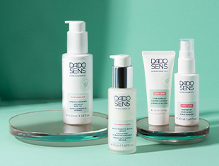 Pflegeprodukte für sensible Haut mit akuten Ausbrüchen, vor türkisfarbenem Hintergrund. Enthält weiße Verpackungen mit türkisfarbenen Elementen.