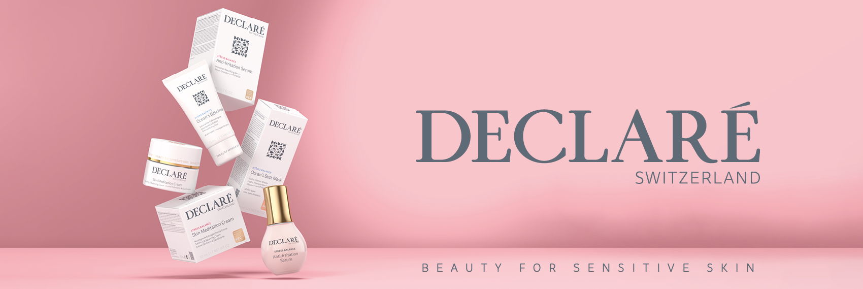 DECLARÉ Switzerland – Pflegeprodukte für empfindliche Haut auf rosafarbenem Hintergrund. Links schweben verschiedene Produktverpackungen und Glastiegel elegant in der Luft. Rechts steht groß das Markenlogo 'DECLARÉ Switzerland'. Am unteren Rand der Schriftzug 'Beauty for Sensitive Skin'.