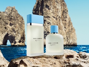 Zwei Flakons des Dolce & Gabbana Light Blue Dufts stehen auf einem Felsen vor einer malerischen Küstenkulisse mit türkisblauem Meer und steilen Felsformationen im Hintergrund.