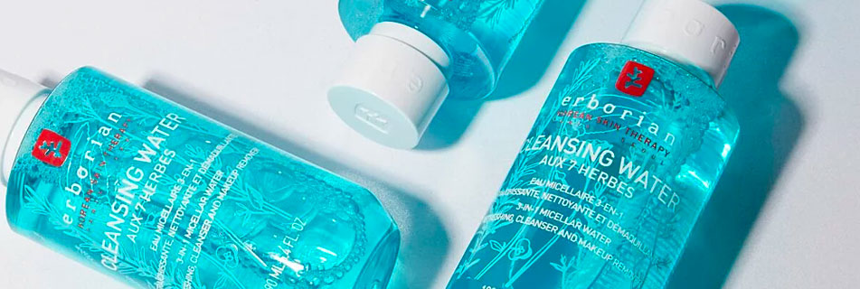 Drei Flaschen Erborian Cleansing Water mit blauer Flüssigkeit und weißem Verschluss, auf einem hellen Hintergrund liegend. Die Etiketten betonen die Formel mit 7 Kräutern zur sanften Gesichtsreinigung.