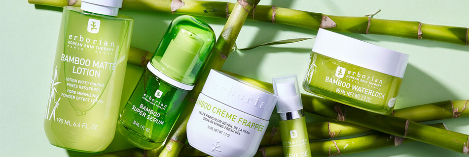 Fünf grüne Hautpflegeprodukte der Bamboo-Serie von Erborian, darunter Lotion, Serum, Crème Frappée und Waterlock, dekorativ arrangiert auf frischen Bambusstäben.
