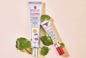 Erborian CC Crème und CC Eye in silberfarbenen Tuben auf pastellfarbenem Hintergrund, dekoriert mit grünen Centella-Blättern.