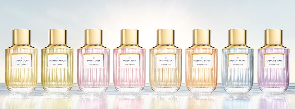 Acht luxuriöse Parfumflakons von Estée Lauder aus der Kollektion mit goldenen Verschlüssen, in zarten Farbverläufen von Gelb, Rosa, Orange, Blau bis Violett. Namen wie Tender Light, Paradise Moon, Dream Dusk und Infinite Sky sind auf den Etiketten sichtbar.