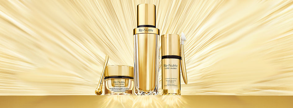 Drei luxuriöse Hautpflegeprodukte aus der Re-Nutriv Serie von Estée Lauder in goldenen Verpackungen, inszeniert vor einem strahlenden goldfarbenen Hintergrund. Enthalten sind eine Creme mit Applikator, ein Serum und eine Augenpflege.