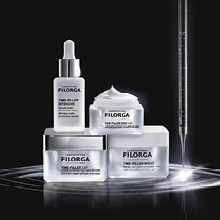 Filorga Time-Filler Pflegeserie bestehend aus vier Produkten: ein Serum mit Pipette, eine Creme mit aufgeschlagener Textur und zwei weitere Cremetiegel. Die Produkte stehen auf glänzender schwarzer Fläche mit einer gläsernen Pipette rechts im Bild, aus der Licht austritt.