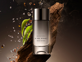 Issey Miyake Le Sel d’Issey Eau de Parfum Flakon vor Holzstruktur mit grünen Blättern und schwebenden Duftnoten