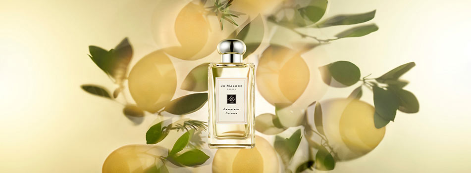 Flakon des Dufts „Grapefruit Cologne“ von Jo Malone London vor gelblich hellem Hintergrund mit Grapefruitfrüchten und grünen Blättern.