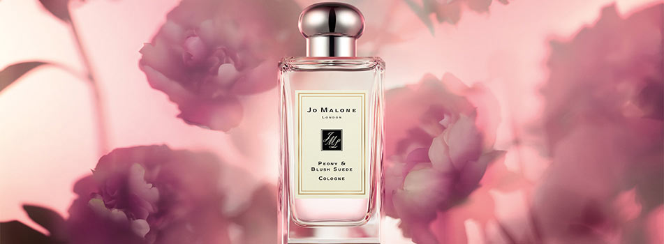 Flakon des Dufts „Peony & Blush Suede Cologne“ von Jo Malone London vor rosafarbenem Hintergrund mit verschwommenen Pfingstrosenblüten.