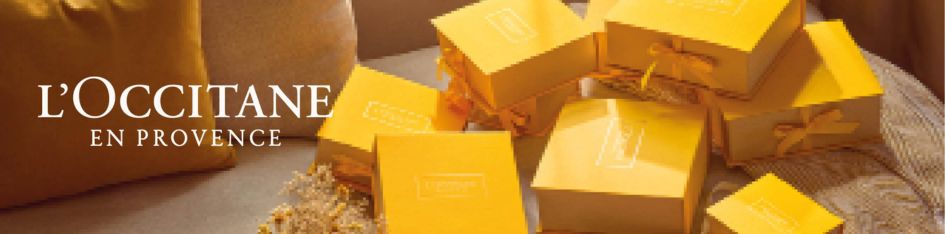 L'Occitane en Provence – Kategoriebanner Geschenke mit gestapelten gelben Geschenkboxen mit Schleife auf warmem Hintergrund