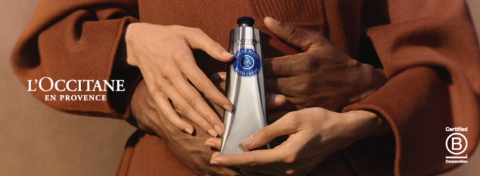 Zwei Hände halten gemeinsam eine silberne Tube L'OCCITANE Handcreme.