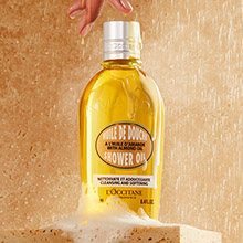 L'OCCITANE Duschöl in einer Flasche mit goldener Flüssigkeit auf einem sandigen Hintergrund.