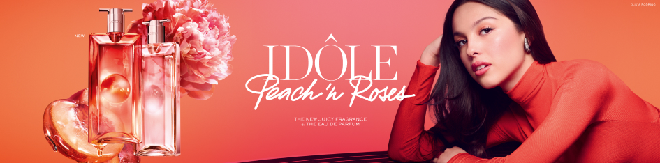 Lancôme Idôle Peach in Roses Eau de Parfum mit zwei rosafarbenen Flakons, Pfingstrose und Model in korallfarbenem Outfit vor warmem Farbverlauf