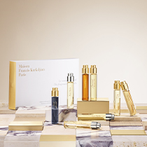 Parfüm-Miniaturen-Set von Maison Francis Kurkdjian Paris. Mehrere schmale, elegante Sprayflakons in Gold, Bernstein, Klar und Dunkelblau stehen auf einer stilvollen Fläche mit Marmor- und Steinmustern. Im Hintergrund eine weiße Box mit goldener Schrift.