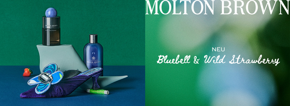 Molton Brown Parfüms und Pflegeprodukte. Im Bild: zwei Flakons, ein dekorativer High Heel mit Schmetterlingsapplikation, eine kleine Erdbeere und Garnrolle. Rechts daneben steht 'Molton Brown – Neu: Bluebell & Wild Strawberry' vor grünem Hintergrund.