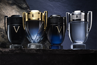 Vier Parfumflakons in Form von Trophäen mit Deckeln und Henkeln stehen nebeneinander auf dunklem Untergrund. Die Flakons sind in verschiedenen Farben und Ausführungen gestaltet: Schwarz mit goldfarbenem V, Gold mit durchsichtigem Glas, Dunkelblau-Schwarz und Silber-Blau.